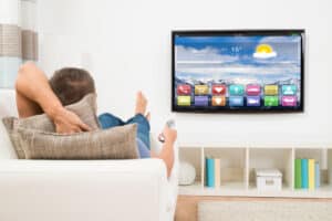 A Man Lying On Sofa Using Remote Control For A Smart Tv